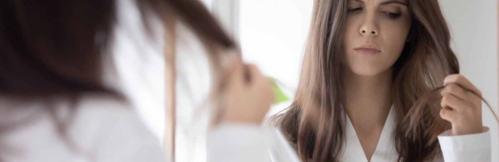 Worried girl concerned about hair loss, combing at mirror, holding hair brush and lock. Upset young woman counting fell out hairs. Haircare, health problem concept. Mirror reflection head shot